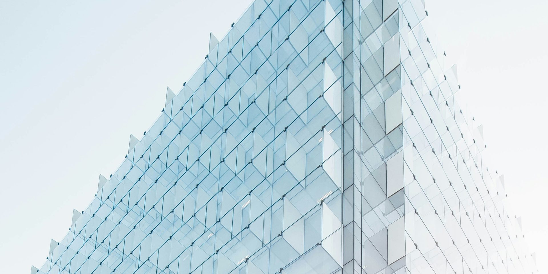 Nowoczesny budynek z przeszkloną fasadą, widok pod kątem, na tle jasnego nieba.